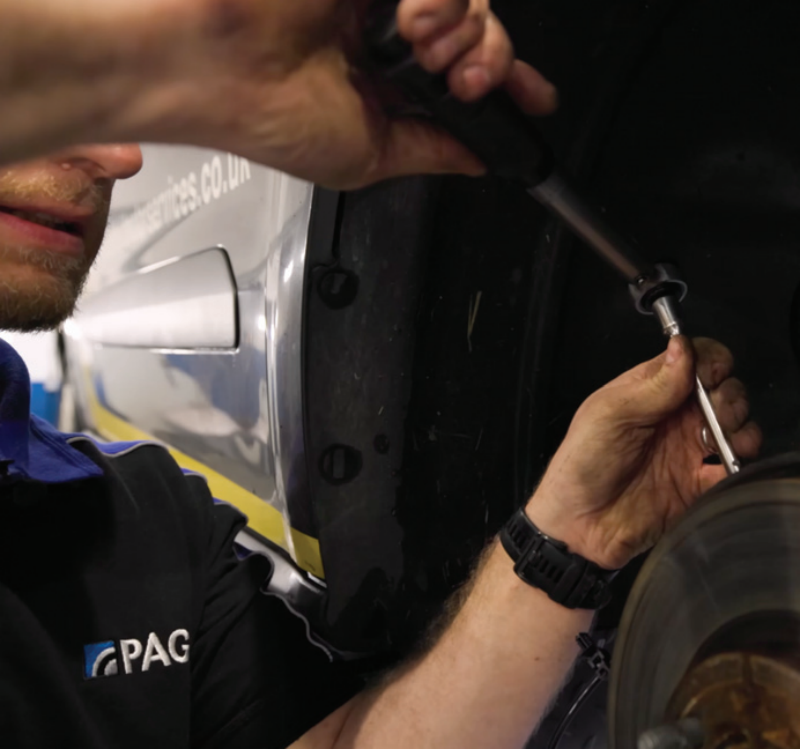 A mechanic in a Pagid uniform using a hand tool to install or tighten an ABS wheel speed sensor behind a car brake disc rotor inside the wheel well.
