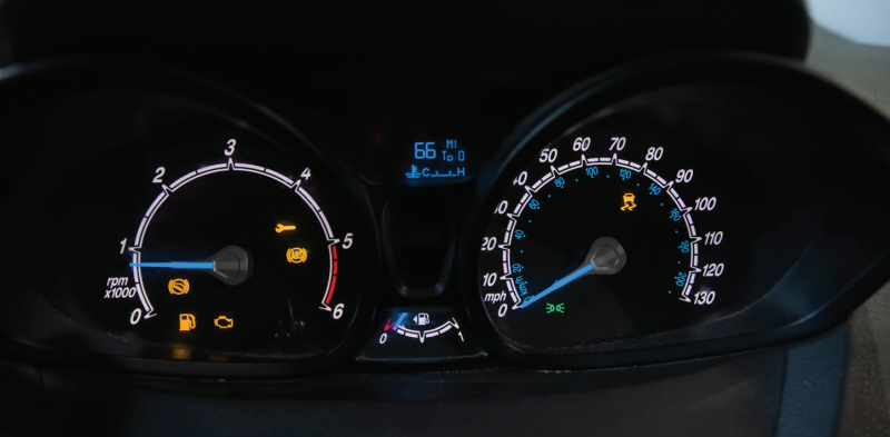 A car dashboard instrument cluster illuminated at night, showing lit warning symbols including the ABS light, traction control malfunction light, hill start assist wrench icon, low fuel light, and check engine light.