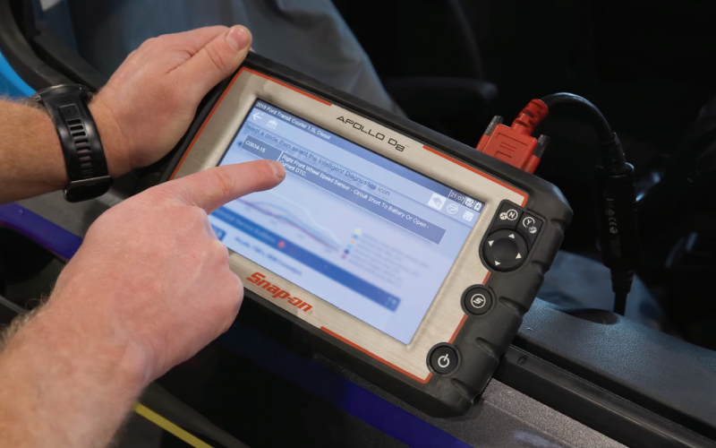 A mechanic pointing at a Snap-on Apollo D8 diagnostic scan tool screen displaying fault code C0034-15 for a right front wheel speed sensor circuit short to battery or open on a 2018 Ford Transit Courier.