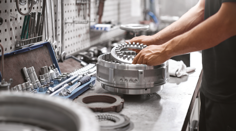 A mechanic working at a well-equipped workbench, assembling or inspecting a complex metallic automotive part.