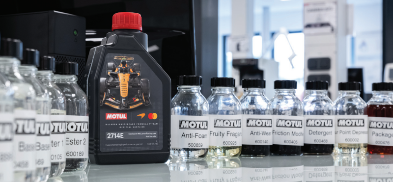 Motul oil additive sample bottles labeled for laboratory testing alongside a branded McLaren Formula One team gear oil container.
