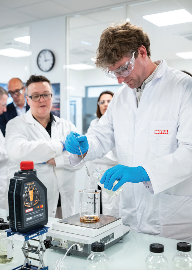 A scientist blending oil additives inside a Motul laboratory while colleagues look on during a technical demonstration.