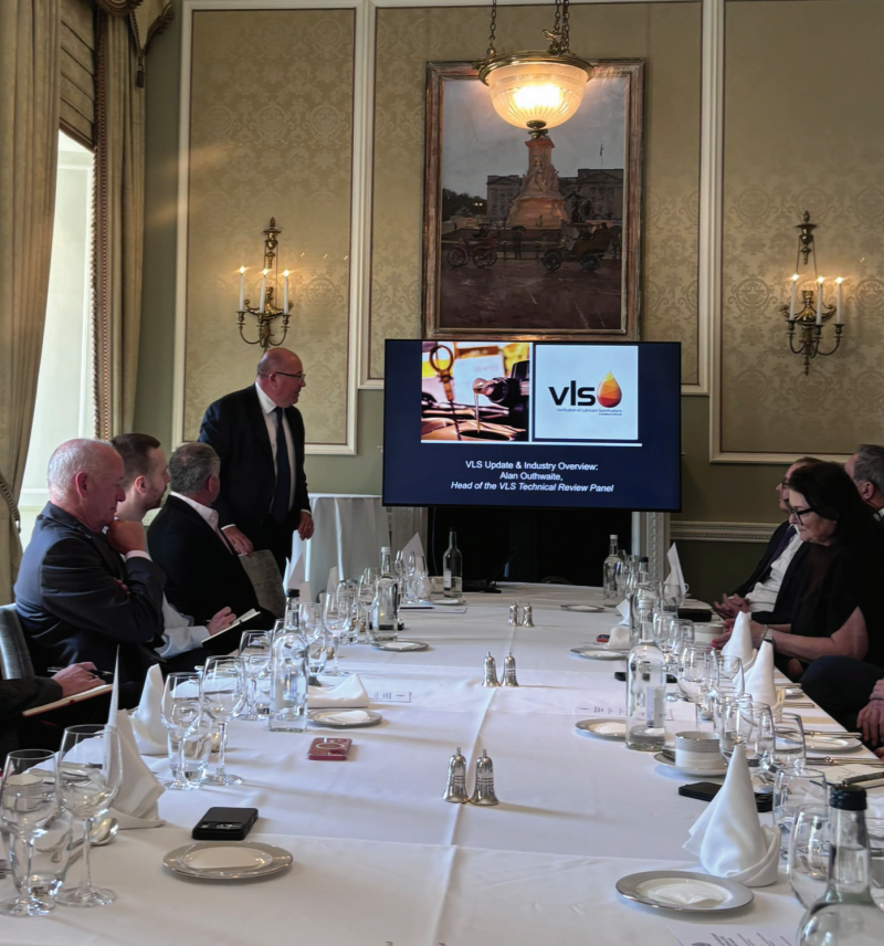 A verification of lubrication specifications presentation shown on a large display screen during an industry meeting at a formal dining venue.