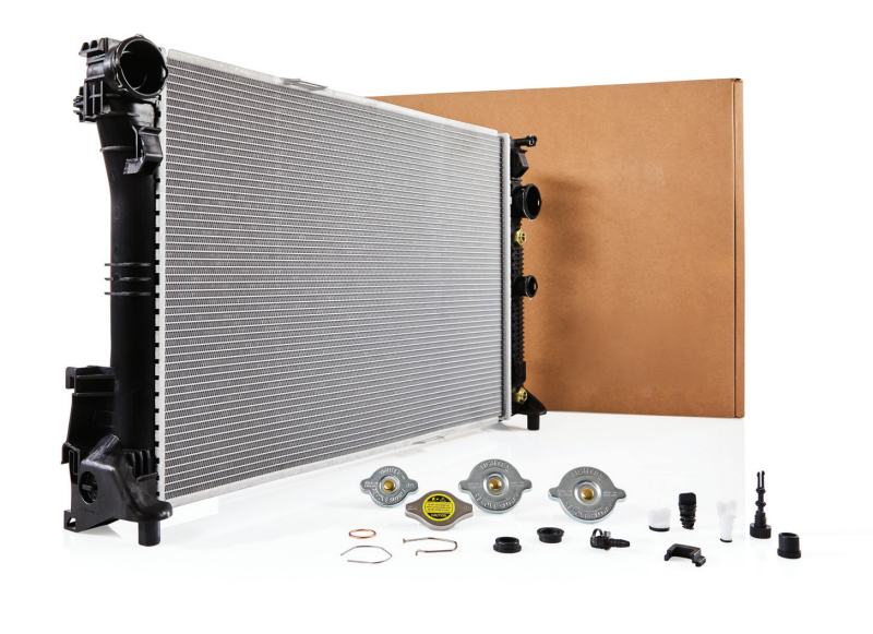A replacement car engine radiator unit shown with its product box, multiple radiator pressure caps, and essential installation hardware components.