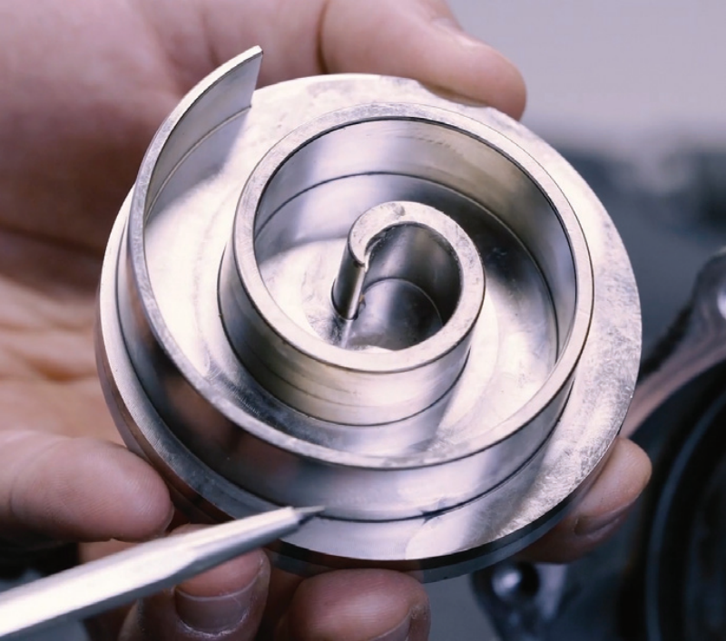 A close-up of a compressor scroll/spiral assembly being inspected with a pointer tool in a workshop setting.