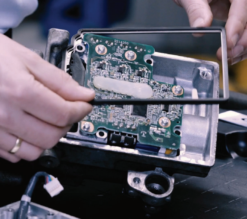 A technician fitting a rubber sealing gasket onto an integrated power inverter module (PIM) of an automotive electric compressor during repair or inspection.
