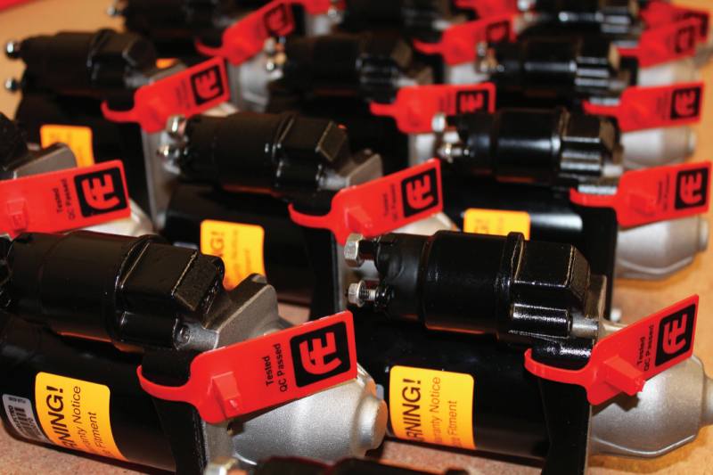 Batch of remanufactured starter motors lined up with red QC Passed tags and yellow warning labels.