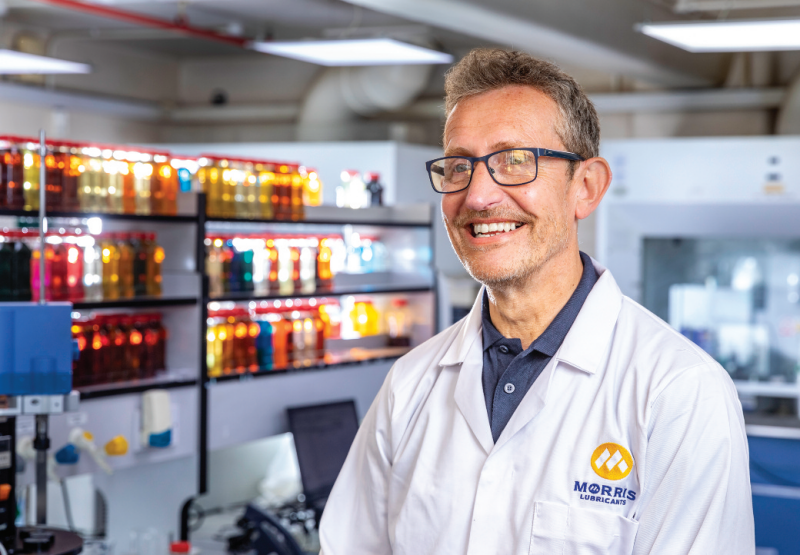 Morris Lubricants laboratory specialist wearing a white lab coat and glasses in a quality control testing facility.