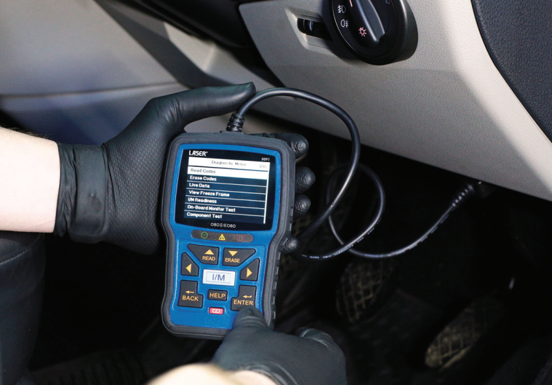 Technician wearing black nitrile gloves operating a Laser OBDII/EOBD handheld diagnostic scan tool plugged into a vehicle's dashboard port.