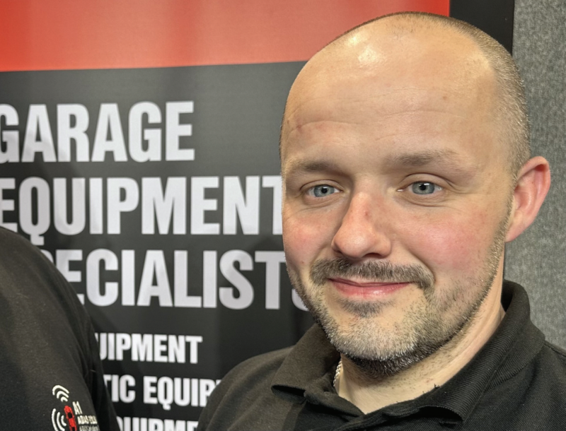 Headshot portrait of a smiling male garage equipment specialist standing in front of a promotional display banner.