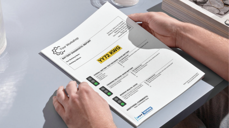 A person holding a printed "Battery Diagnostic Report" from "Your Workshop" featuring vehicle registration YY72 KWG, displaying overall "Good Battery" test results with green indicator lights for overall status, cranking decision, and reserve health, alongside an IAM Robis logo at the bottom.