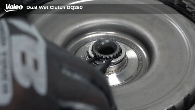 Close-up, top-down view of a Valeo Dual Wet Clutch DQ250 transmission assembly, with a technician using specialized pliers to service the internal snap ring and splined hub components.