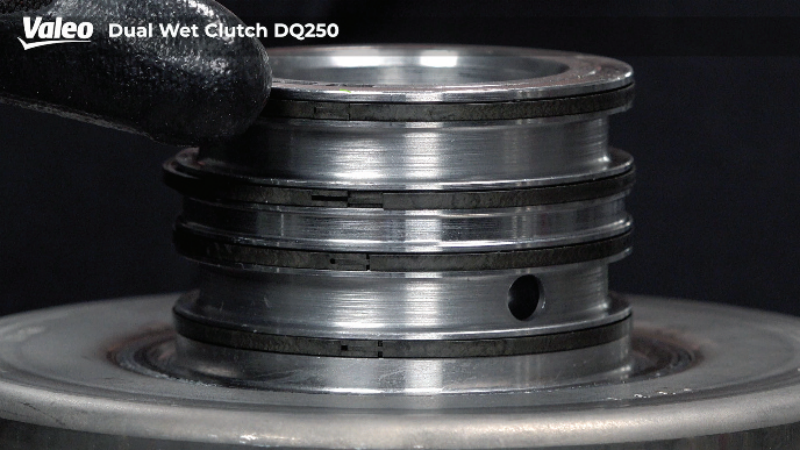 Close-up studio view of the Valeo Dual Wet Clutch DQ250 assembly showing stacked sealing rings on the hydraulic piston hub, with a gloved hand pointing at the upper ring channel. 