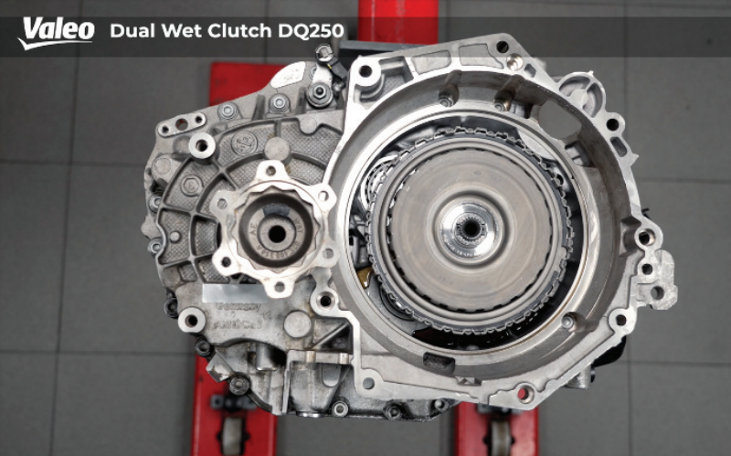 Top-down view of the completed Valeo Dual Wet Clutch DQ250 assembly mounted securely on a red workshop stand over a grey tiled floor, showing the reinstalled clutch pack, internal housing components, and differential output flange.