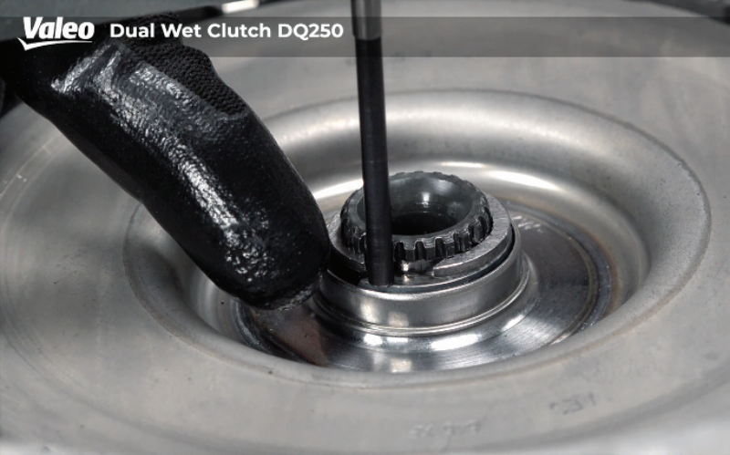 Extreme close-up view of the Valeo Dual Wet Clutch DQ250 assembly showing the dial indicator plunger resting directly against the central hub and release bearing race, with a gloved hand stabilizing the area during axial play measurement.