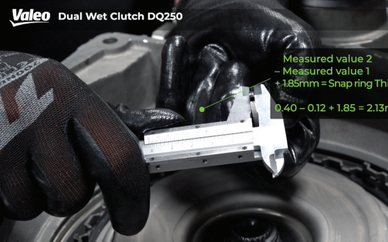Close-up view of a technician wearing black work gloves measuring a snap ring with a vernier caliper above the Valeo Dual Wet Clutch DQ250 assembly, featuring an overlay formula for calculating required snap ring thickness