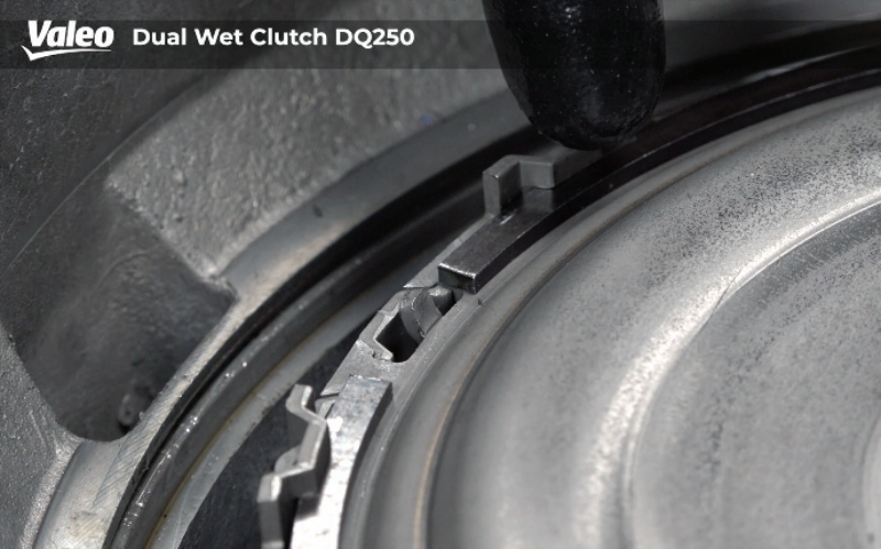 Extreme close-up studio view of the Valeo Dual Wet Clutch DQ250 assembly showing a gloved hand positioning or checking the interlocking snap ring segment seated within the outer housing groove.